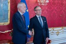 Foto: Österreichs Bundespräsident Alexander Van der Bellen und Herbert Kickl geben sich vor einer EU-Fahne in einem prunkvollen Raum die Hand.