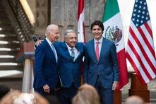 Foto: Joe Biden, Andrés Manuel López Obrador und Justin Trudeau stehen nebeneinander, lächeln und umarmen sich vor  Flaggen der USA, Mexiko und Kanada.