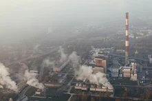 Photo: Aerial view of an industrial area with factories and smoking chimneys. A tall red-and-white striped chimney stands out.