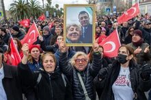 Foto: Eine Menschenmenge mit türkischen Flaggen protestiert auf einer Straße. Eine Person hält ein gerahmtes Foto von zwei Menschen hoch.