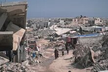 Foto: Zerstörte Gebäude und Trümmer in Gaza, mehrere Personen gehen eine staubige Straße entlang.