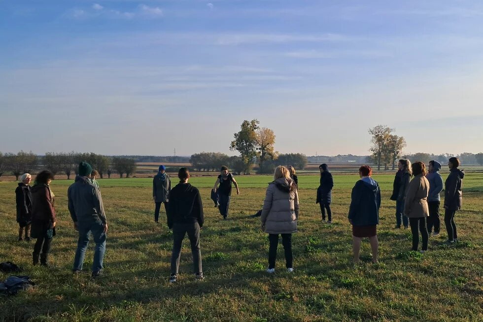 Gathering of female agroecological farmers from Central and Eastern Europe in Grzybów, Poland, October 2024. Photo: A group of people stand in a circle in a meadow. Fields, trees and a clear sky can be seen in the background.